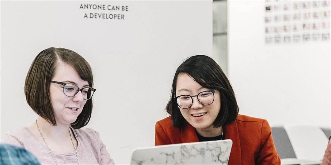 Two students smiling around laptop