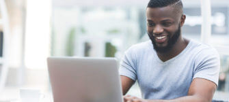 Smiling man text messaging on laptop in cafe